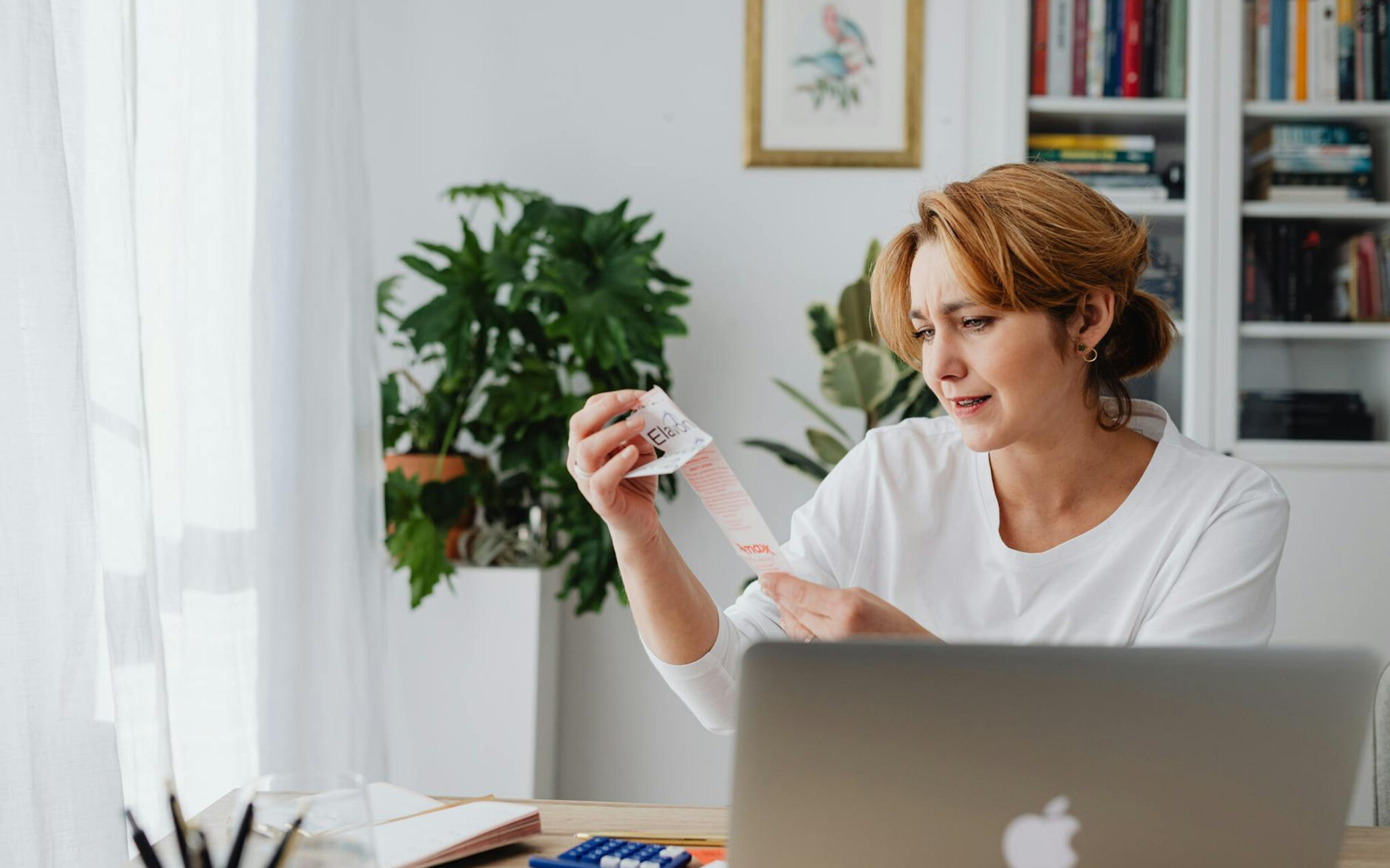 Concerned woman reviewing a long receipt at home with a laptop and calculator, representing financial stress due to inflation.