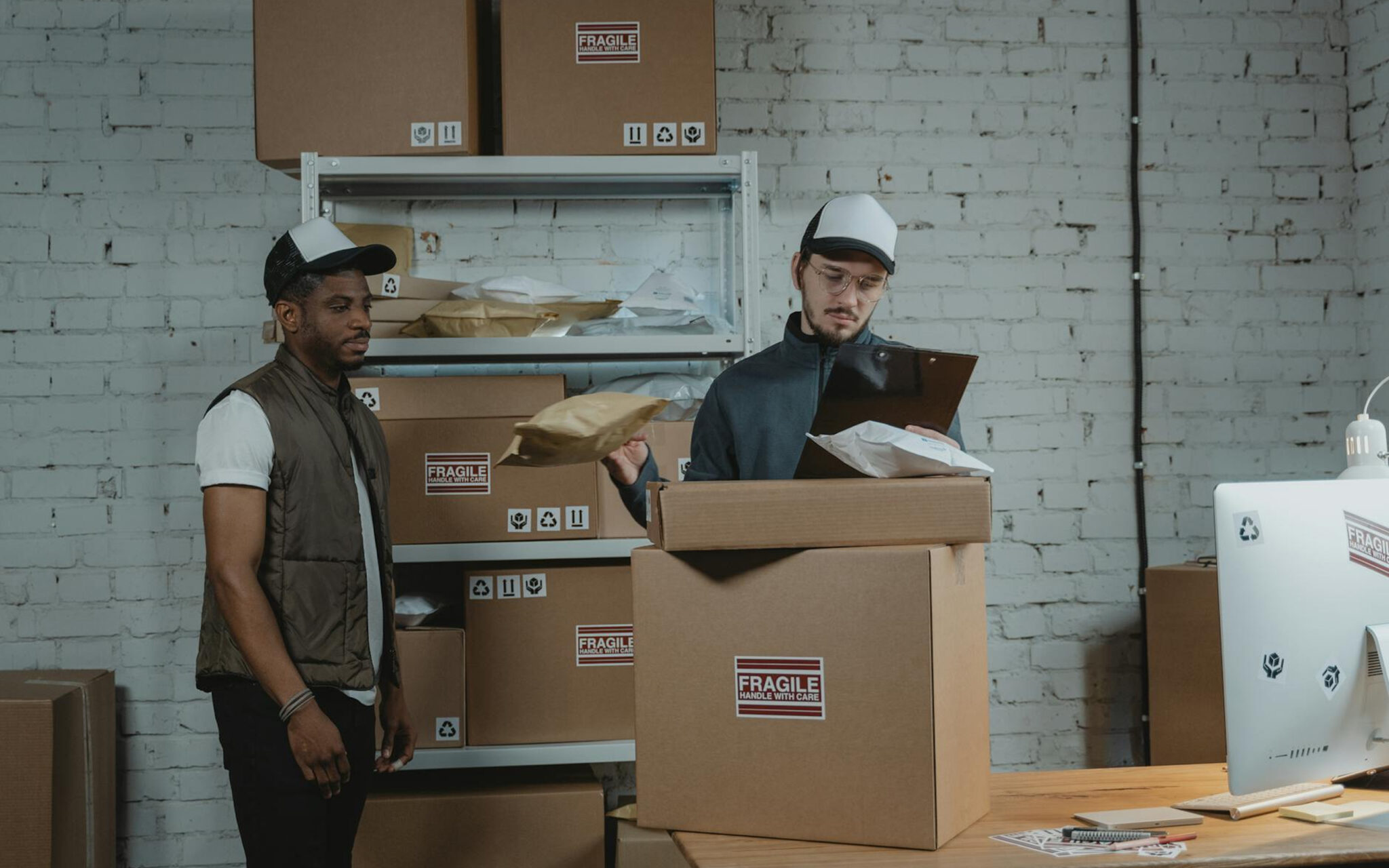 Two warehouse workers preparing shipments and checking inventory with cardboard boxes in a packing station.